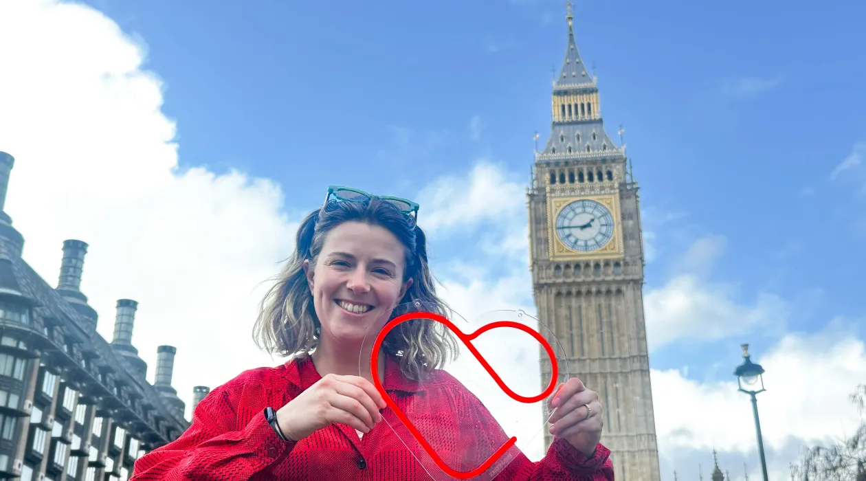 A woman holding a HeartLab heart-shaped sign in front of Big Ben in London