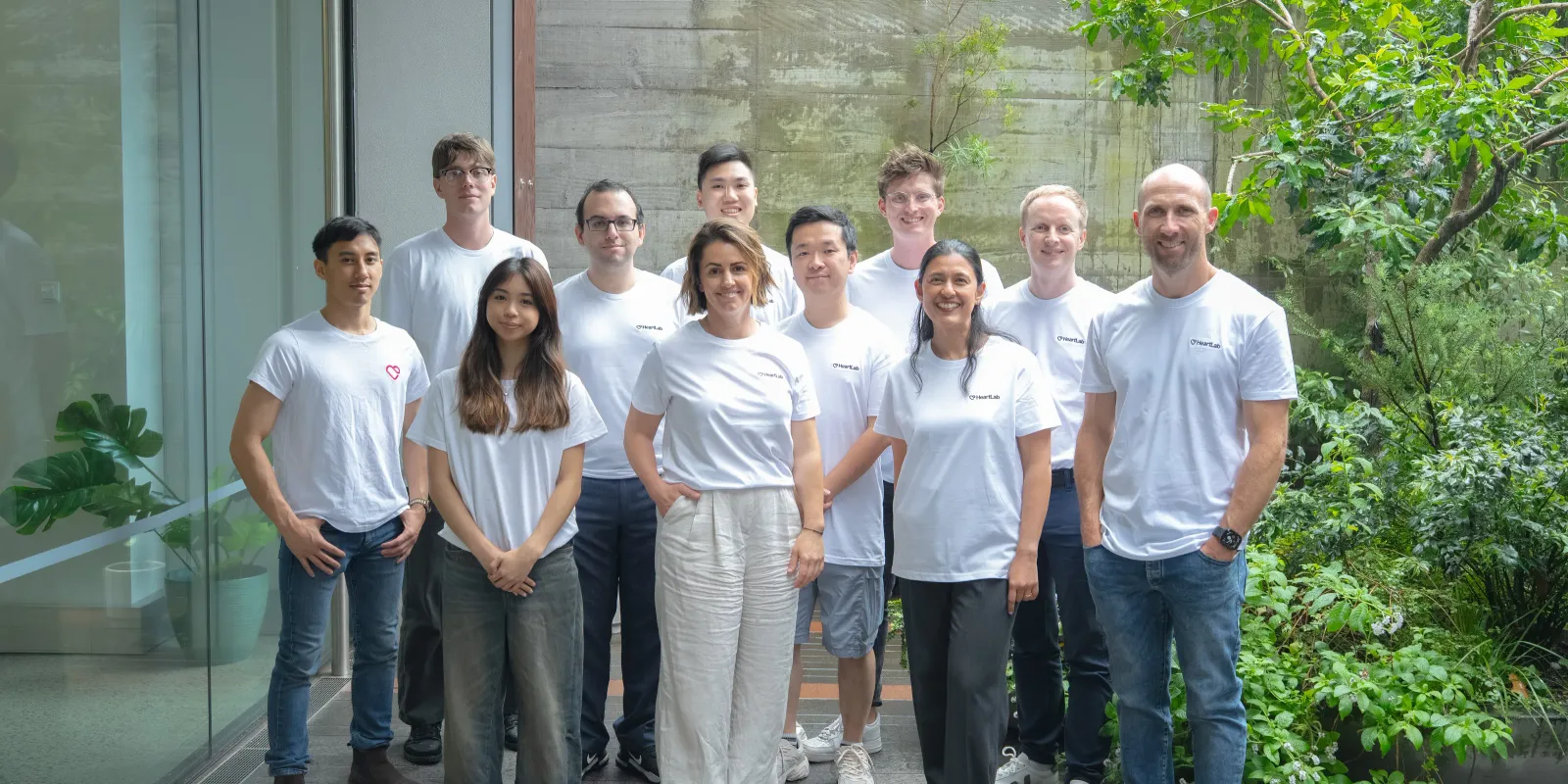 Eleven members of the HeartLab team standing together in the planted courtyard outside the office